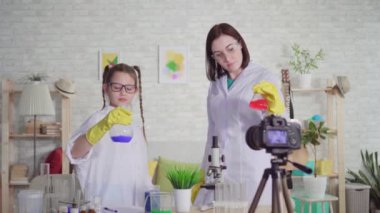 Genç bir kadın ve genç bir kız blogcu, kimya laboratuvarında, okul projesi reaksiyonlarında ve beş dakika içinde kameraya bakın.