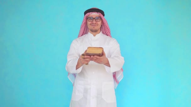 Arabský muž s růžovou a knihou v dlaních stojí na modrém pozadí — Stock video
