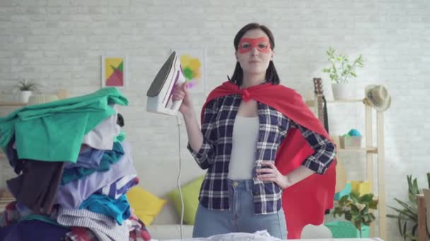 Porträt einer Hausfrau Superheldin mit dem Bügeleisen in der Hand neben einem Bügelbrett — Stockvideo