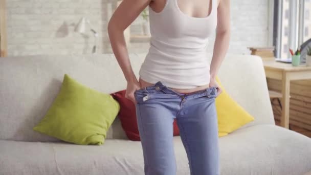 Крупным планом молодая женщина пытается надеть джинсы, потому что набирает жир на бедрах . — стоковое видео