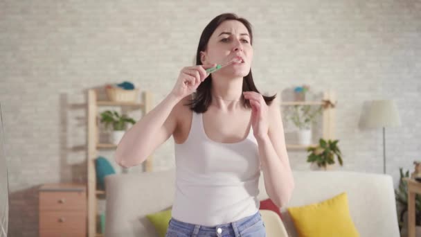 Молодая женщина замечает кровь на щетке и во рту, когда чистит зубы. — стоковое видео