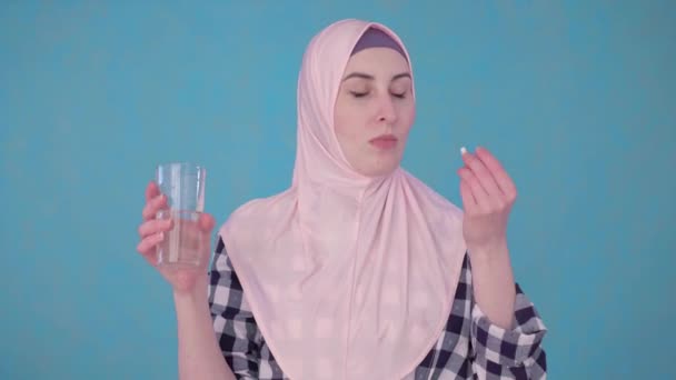Young beautiful Muslim woman with a pill and a glass of water taking a pill — Stock Video