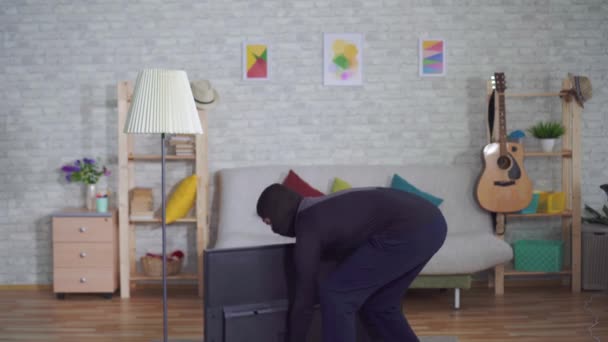 Анонимный вор в маске балаклавы крадет телевизор в доме и испытывает боль в спине — стоковое видео