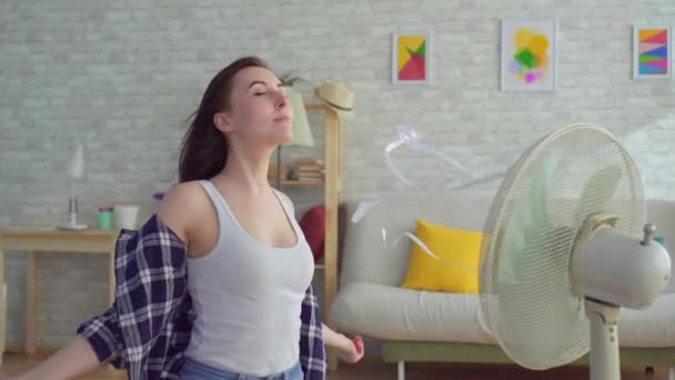 Young woman sitting in living room with electric fan — 비디오