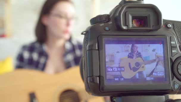 Giovane blogger donna, seduta sul divano a suonare la chitarra scattata attraverso lo schermo della fotocamera — Video Stock