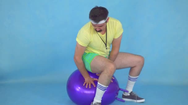 Hombre atlético divertido en el estilo de los años 80, saltando en la pelota para la aptitud — Vídeos de Stock