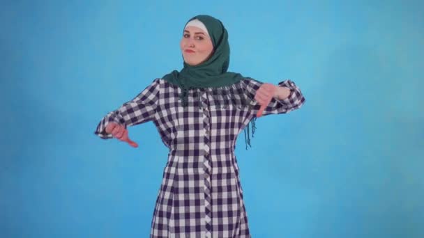 Young Muslim woman showing thumb down on blue background — Stock Video