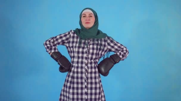 Mujer musulmana joven en guantes de boxeo sobre un fondo azul mira a la cámara — Vídeos de Stock