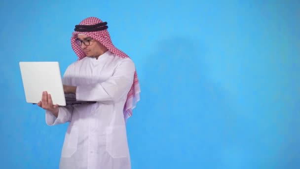 Arab man på en isolerad blå bakgrund med laptop tittar på kamera — Stockvideo