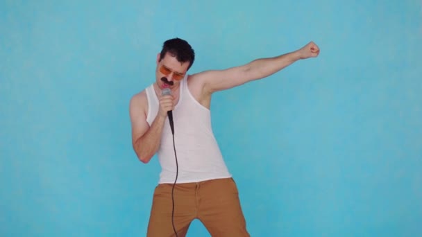 Chantant drôle jeune homme avec microphone à la main sur fond bleu — Video