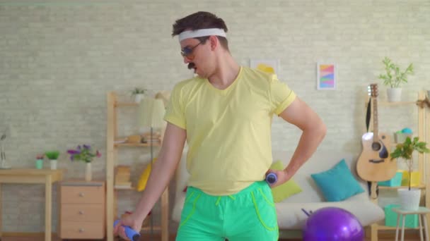 Lustiger athletischer Mann im Stil der 80er Jahre ist mit Hanteln beschäftigt und posiert vor der Kamera — Stockvideo