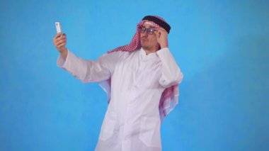 Arap adam mavi arka plan üzerinde akıllı telefon kamerası bir selfie alır