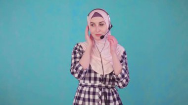 Telefon kulaklığı takmış, kameraya bakıyor ve gülümsüyor.