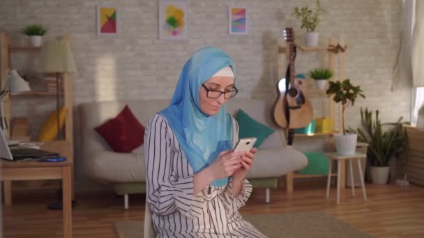 Ung muslimsk kvinde i hijab med et ar fra en forbrænding på hendes ansigt bruger en smartphone – Stock-video
