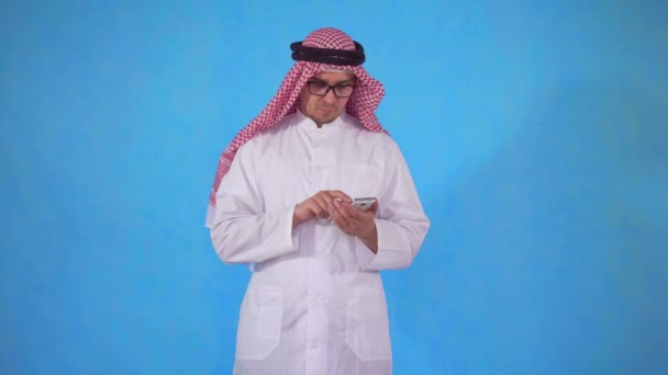 Arab mężczyzna używa smartfona na niebieskim tle — Wideo stockowe