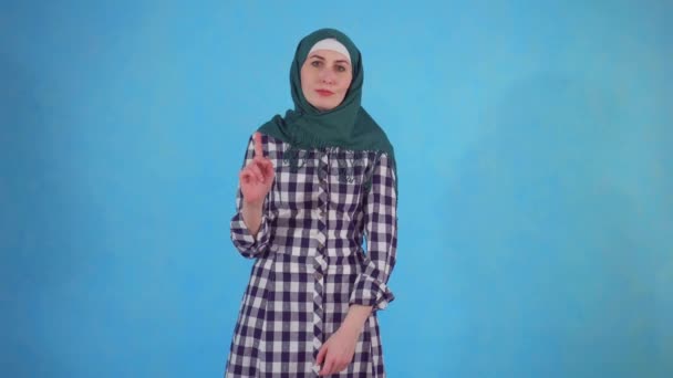 Junge muslimische Frau drückt Missbilligung auf blauem Hintergrund aus — Stockvideo
