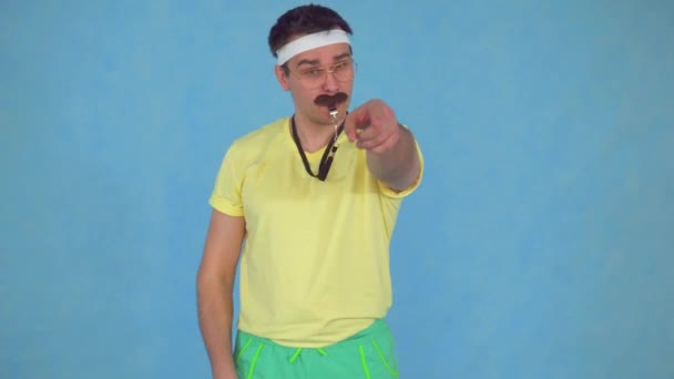 Hombre divertido entrenador con un silbato con un bigote de los 80, sobre un fondo azul — Vídeos de Stock