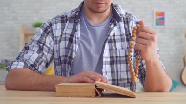 Acercamiento de un joven con un rosario en las manos, leyendo la Biblia — Vídeo de stock