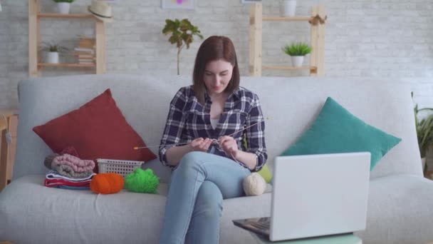 Frau sitzt auf der Couch vor dem Laptop und lernt Stricken — Stockvideo