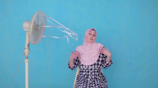Młoda muzułmanka w hidżabie cierpiąca na gorącą pogodę chłodzona przez wentylator — Wideo stockowe