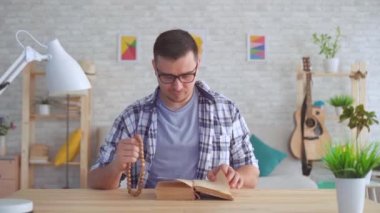 Elinde tespih olan ve masada İncil olan inanan genç adam kameraya bakıyor.