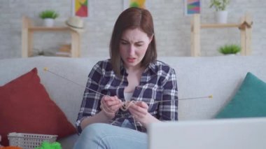 Kadın dizüstü bilgisayarın önünde oturmuş örgü videosu seyrediyor ve işe yaramıyor.