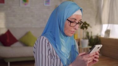 Yüzünde ki yanıktan yara izi olan türbanlı genç müslüman kadın akıllı telefon kullanıyor