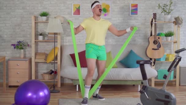 Homem engraçado perdedor que faz fitness em casa com a ajuda de bandas elásticas slow mo — Vídeo de Stock