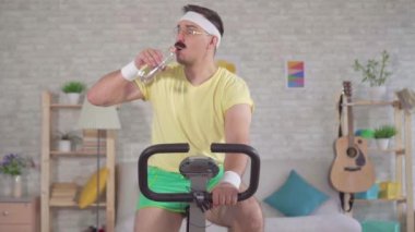 Bir egzersiz bisikleti ve içme suyu yavaş mo evde meşgul bir bıyık ile 80'li komik adam atlet