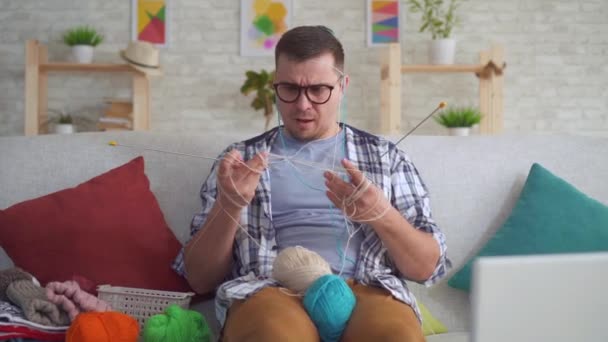 Clumsy young man with glasses knitting needles — Stock Video