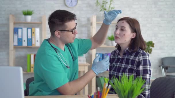 Läkare undersöker en ung kvinna med stora mullvadar på hennes ansikte och ger rekommendationer — Stockvideo