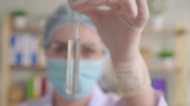 Bir kimya laboratuvarında uzun cam bir pipetle test tüpüne kırmızı sıvı atan genç bir kadın.