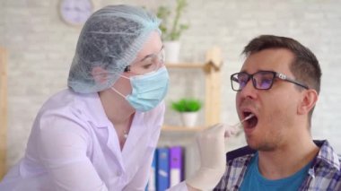 Kadın laboratuar teknisyeni, bir erkeğin ağzından tükürük testi yapıyor.