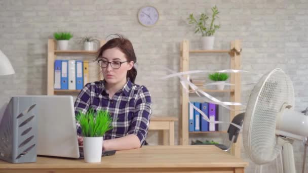 Ung kvinna som arbetar på en bärbar dator bredvid en fläkt flyr från värmen slow mo — Stockvideo