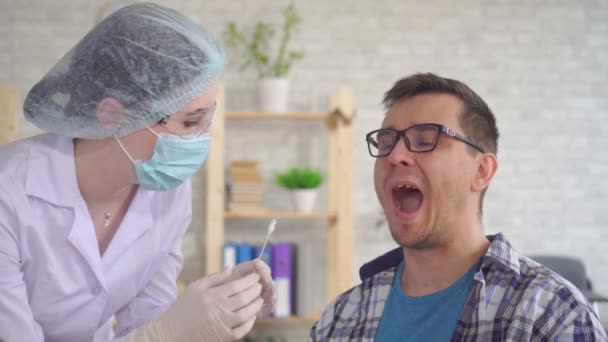 Técnico de laboratorio tomando una prueba de saliva de la boca de un hombre con un hisopo de algodón — Vídeos de Stock