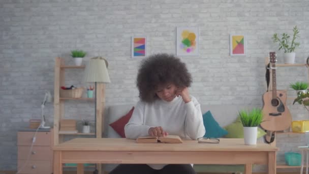 Mujer afroamericana con un peinado afro leyendo un libro en la mesa — Vídeos de Stock