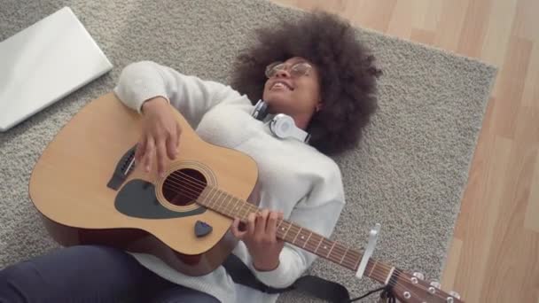 Mulher americana africana bonita com um penteado afro deitado no chão tocando guitarra vista superior — Vídeo de Stock