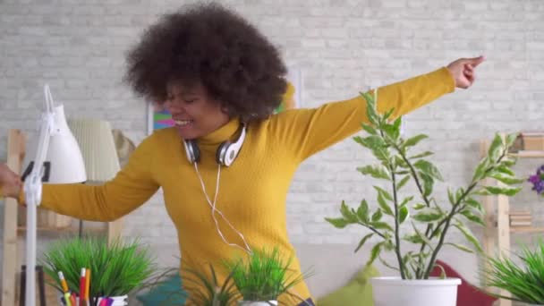 Expresiva bailando positiva Hermosa mujer afroamericana con un peinado afro cuida flores y plantas en apartamentos modernos — Vídeos de Stock