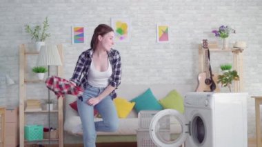 neşeli genç kadın ev hanımı modern dairede giysi ve dansları yıkıyor