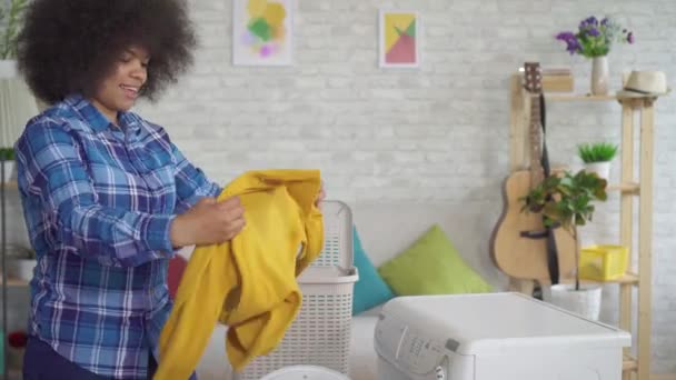 Portret African American gospodyni domowa w koszuli robi pracę domową, biorąc na zewnątrz umyte ubrania w domu — Wideo stockowe