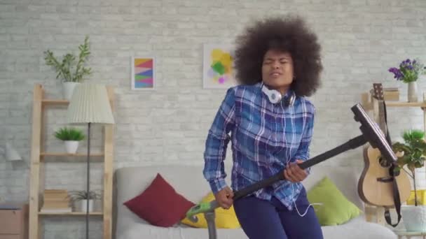 Expressivo positivo afro-americano jovem dona de casa aspirando canta diversão dançando e tocando guitarra imaginária — Vídeo de Stock