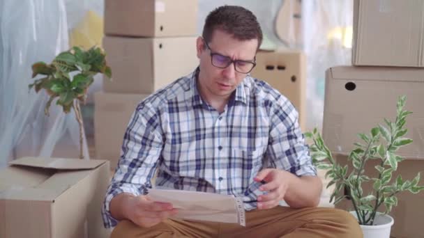 Hombre de mediana edad cansado y molesto con gafas entre las cajas para mover, lee los documentos para el desalojo — Vídeos de Stock