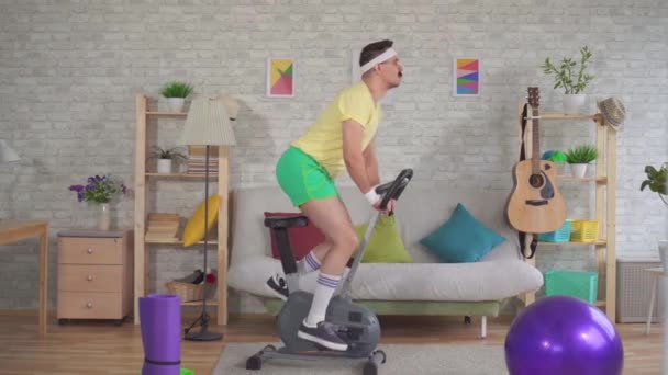 Grappige atleet uit de jaren 80 met een snor is bezig met een hometrainer in het appartement — Stockvideo