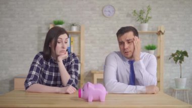 Evli çift masada evde oturur ve kumbara şaşkın görünüyor