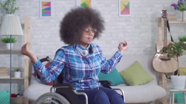 Mulher africana com deficiência alegre com um penteado afro dançando sentado em uma cadeira de rodas slow mo — Vídeo de Stock