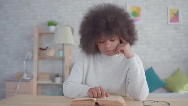 Portré afroamerikai nő egy afro frizura olvasatban egy könyvet az asztalnál — Stock videók