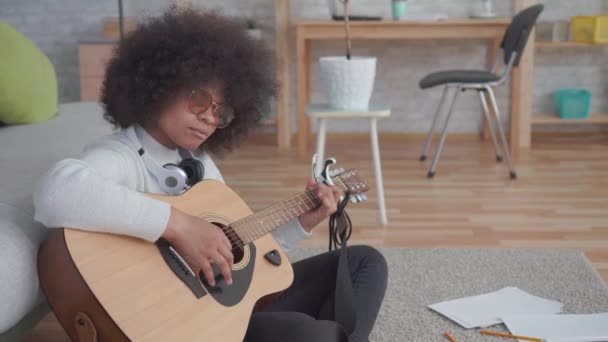 Portrait african american woman with an afro hairstyle plays guitar sitting on the floor — Stock Video