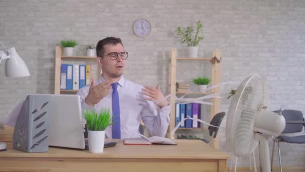 Jongeman werkt aan een laptop in het kantoor zittend voor de ventilator — Stockvideo