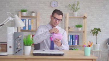 Adam ofiste oturan ve domuzcuk banka kamera bakarak içine bir sikke atar ve parmağını gösterir