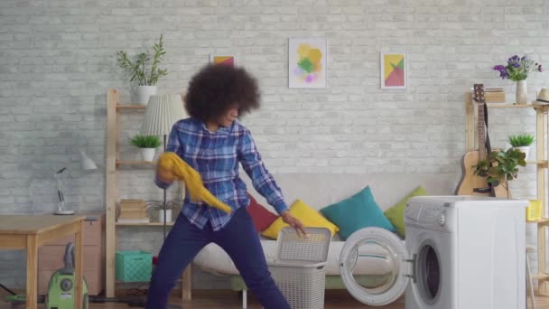 Mujer africana feliz con un peinado afro arroja ropa sucia en la lavadora como una pelota en la cesta lenta mo — Vídeo de stock